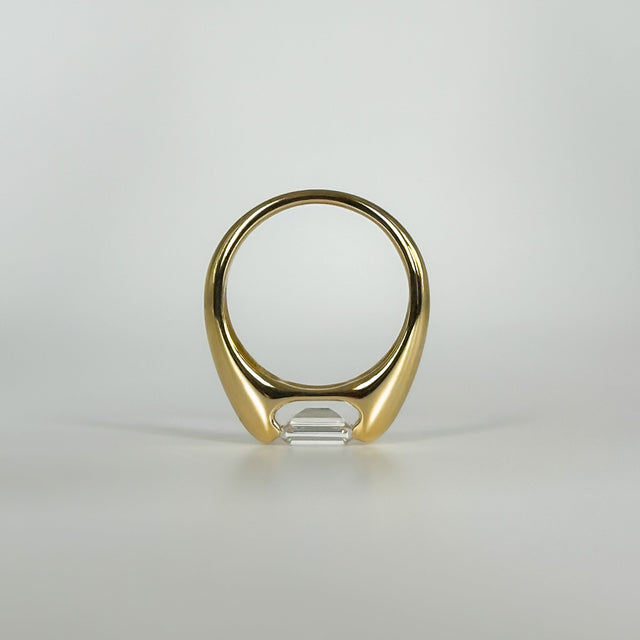 Gold ring with an emerald cut diamond on a light gray background
