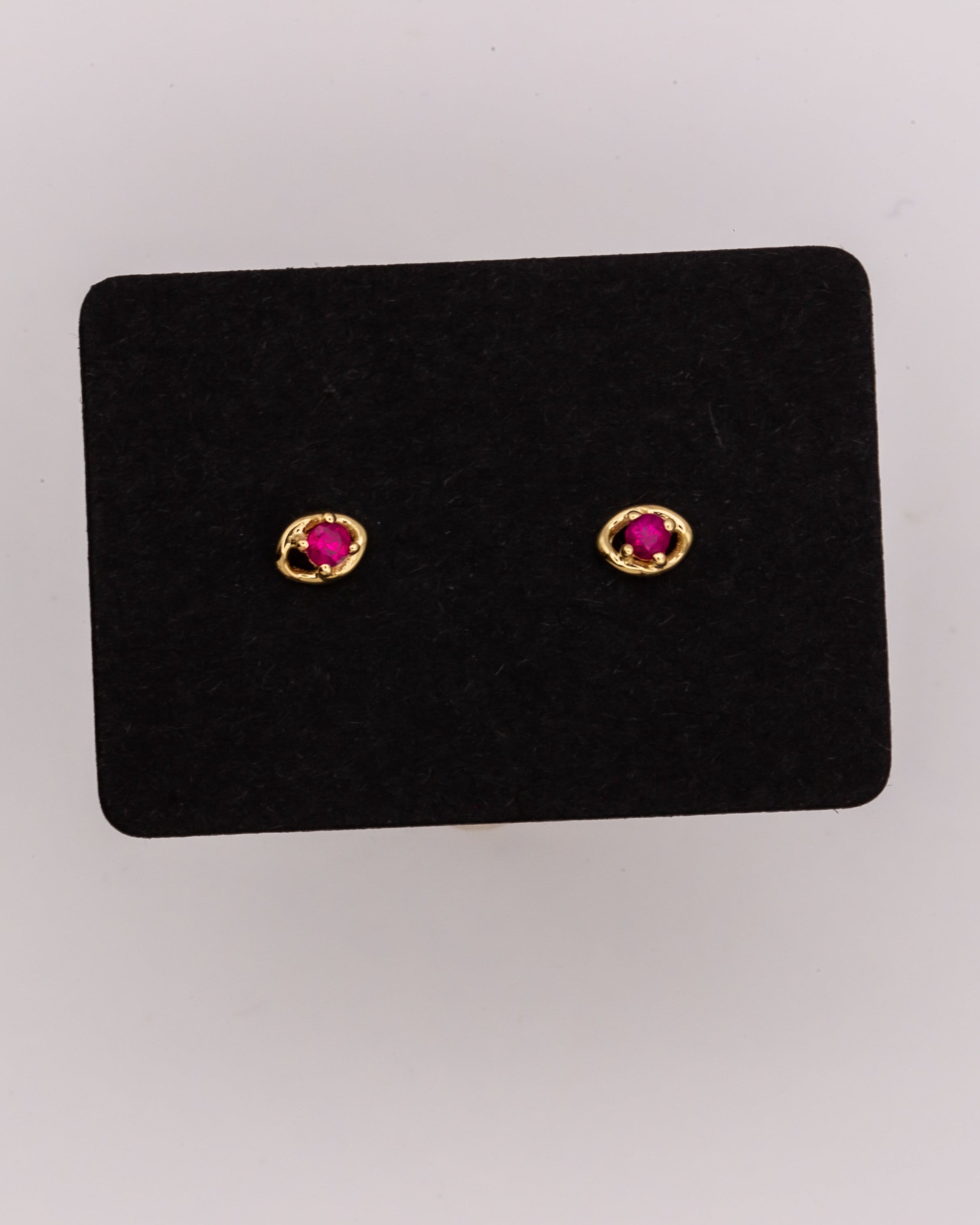 Pair of gold earrings with rubies on a black stand against a light gray background