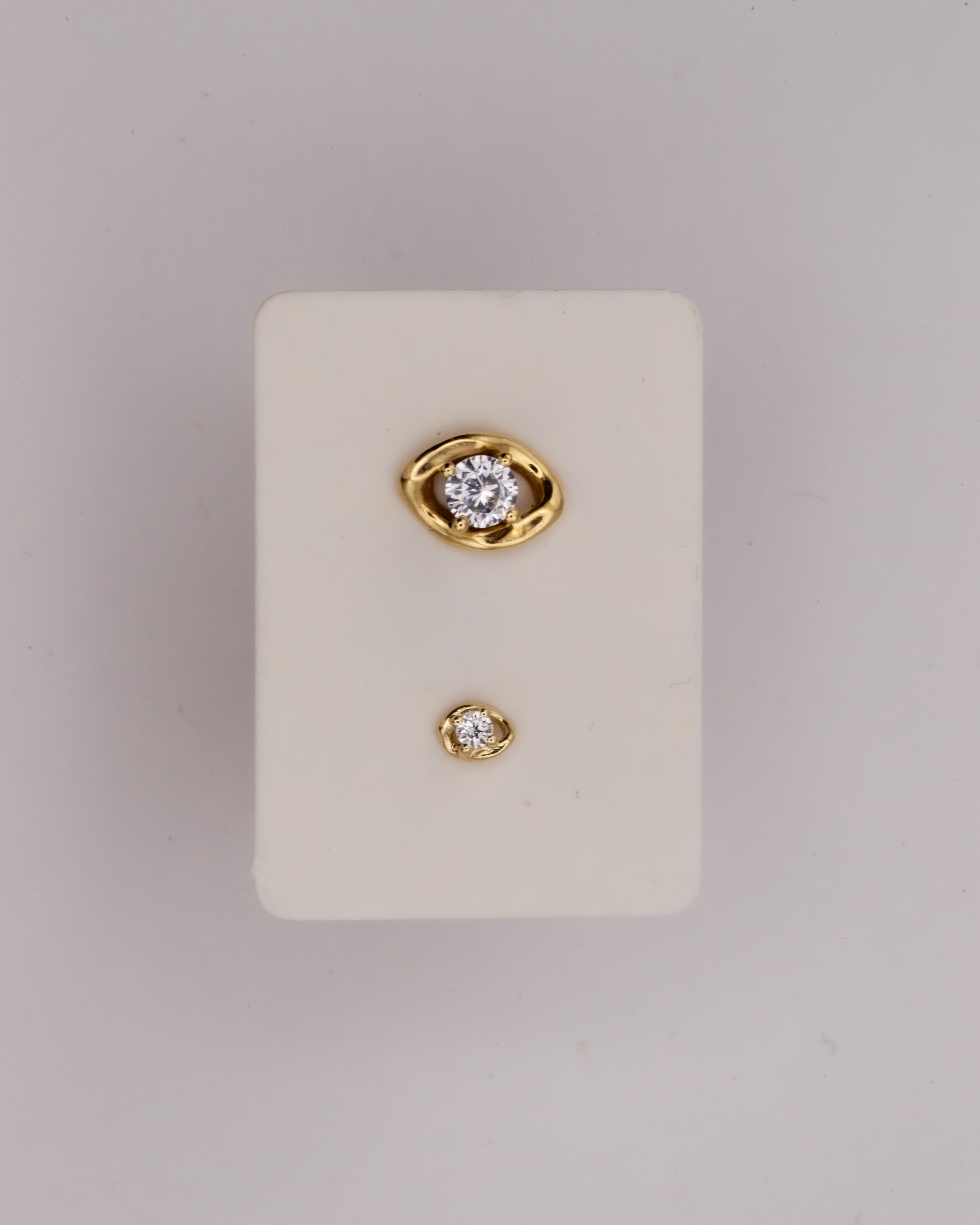 Gold earrings with diamonds on a white card against a light gray background