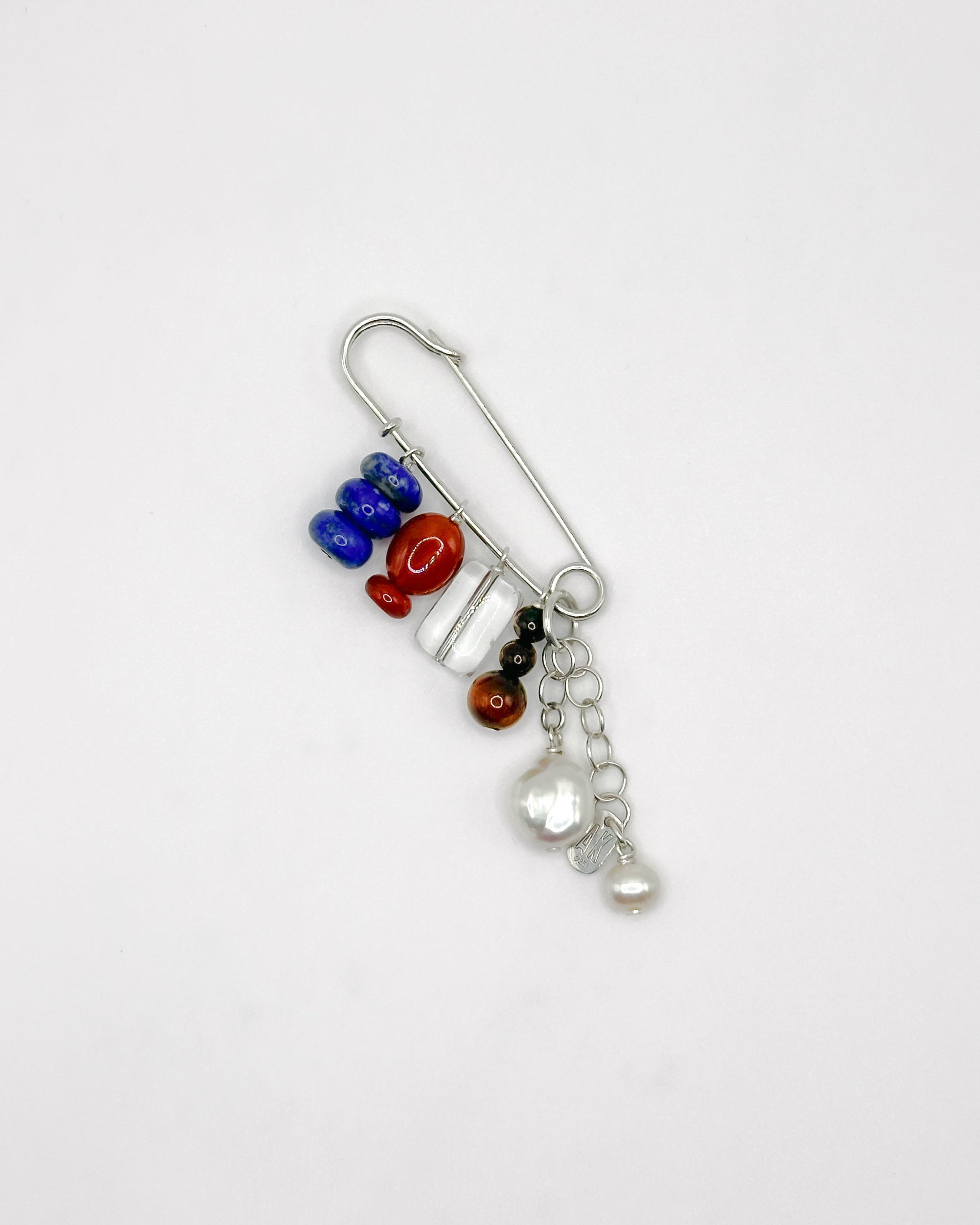 Decorative brooch with colorful stones and a pearl charm on a white background