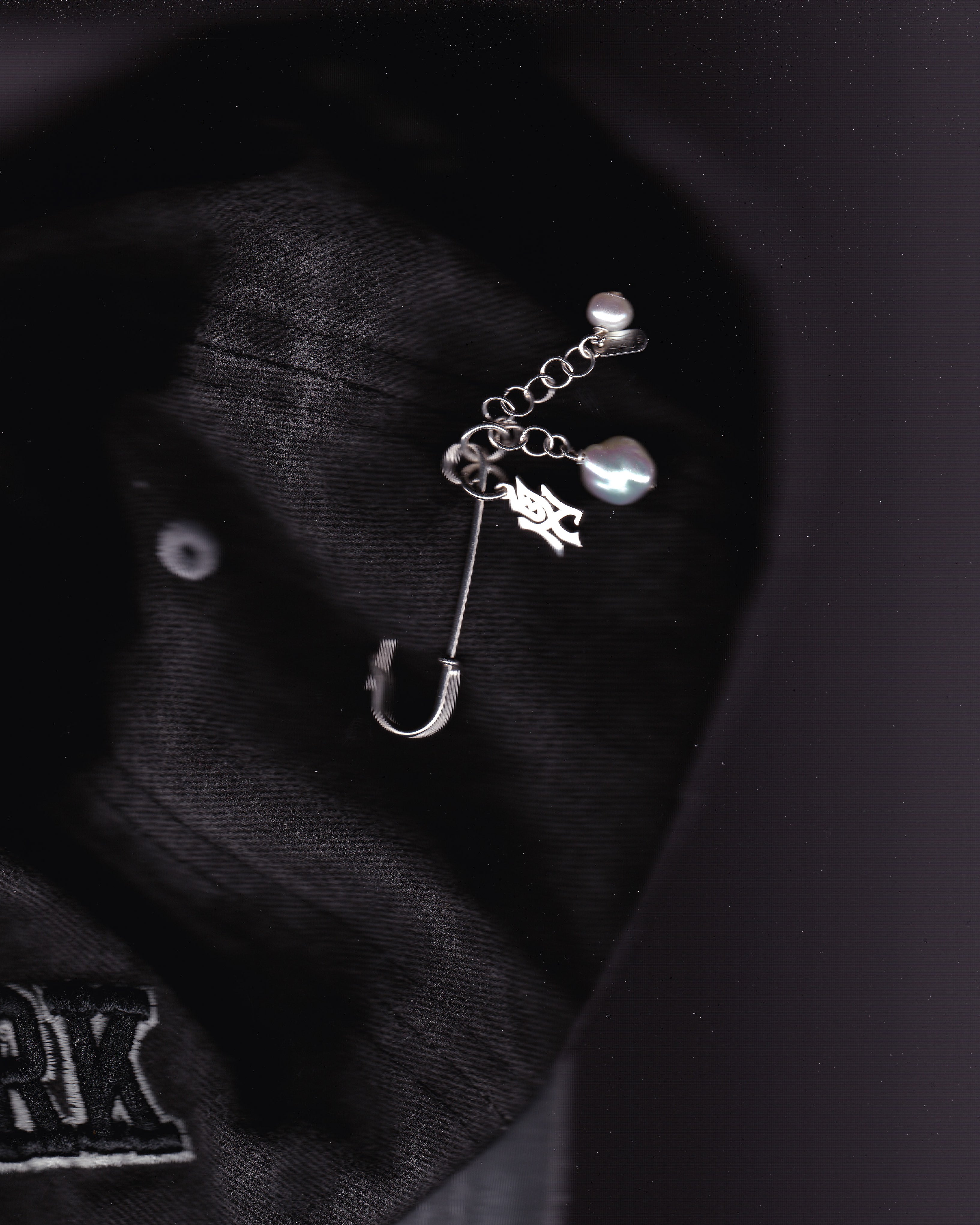 Silver safety pin with charms on a black baseball hat