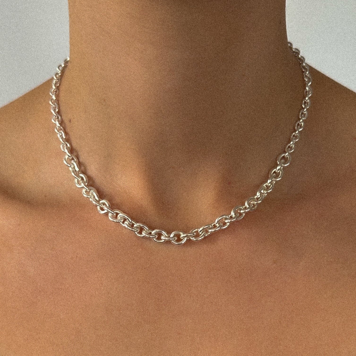 Silver chain necklace on a person's neck against a neutral background