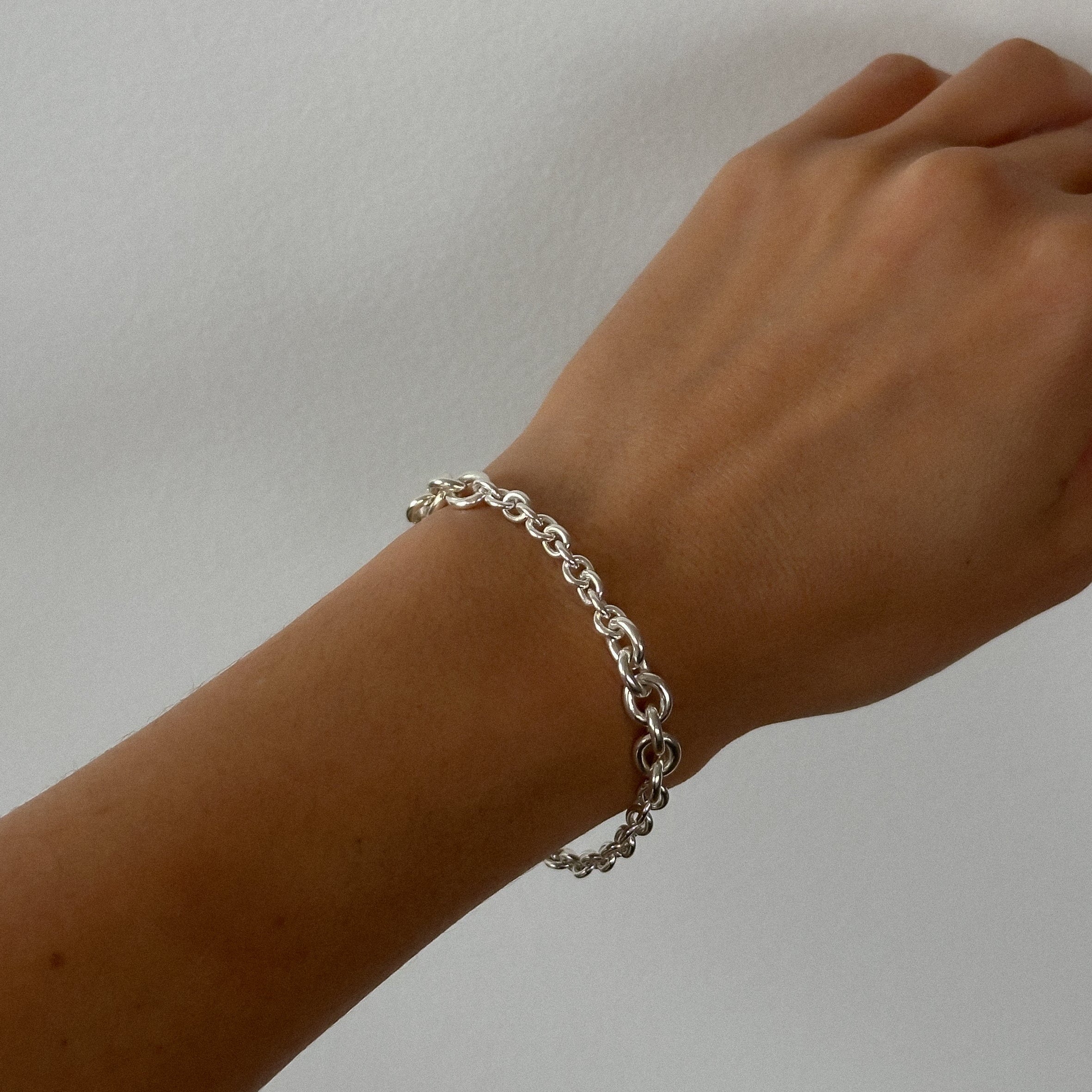 Silver chain bracelet on a wrist against a plain background