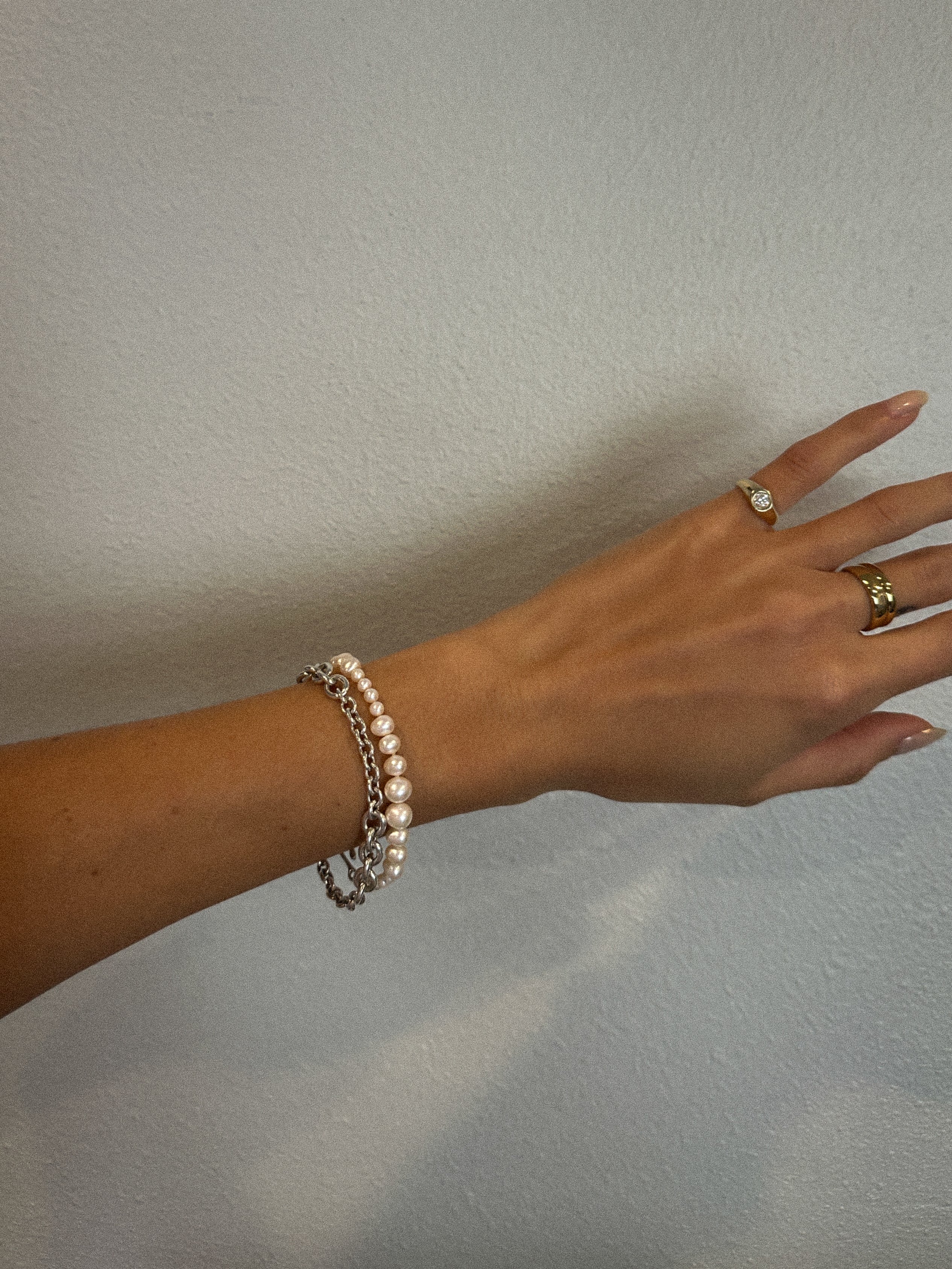 Hand wearing a graduating pearl bracelet on a plain background