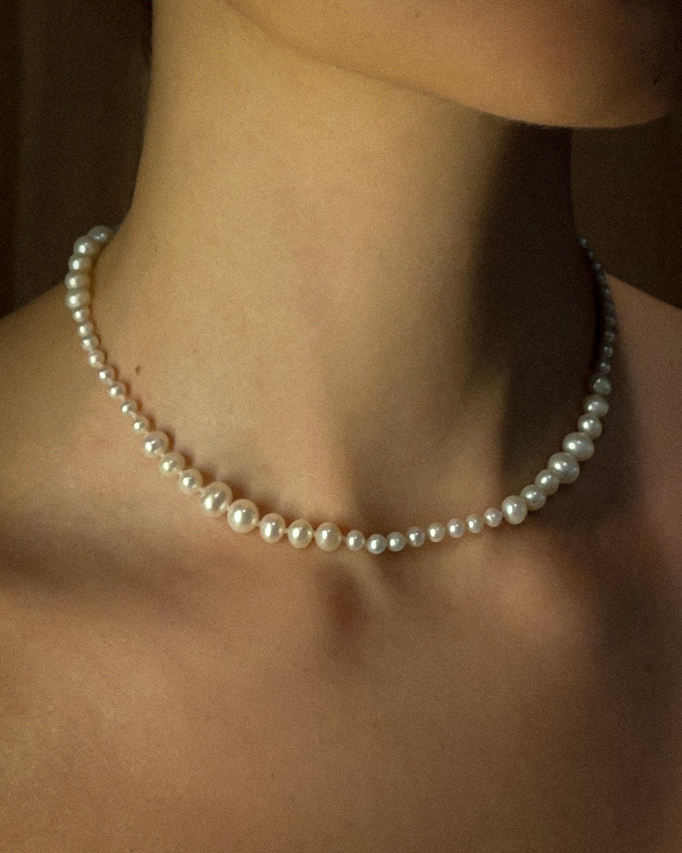 Graduated pearl necklace being worn on a person's neck with a blurred background