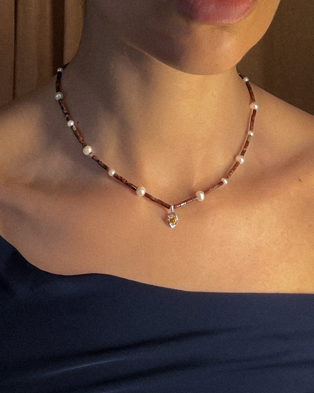 Jasper necklace with pearls and a small white cold and citrine pendant on a person wearing a dark blue top.