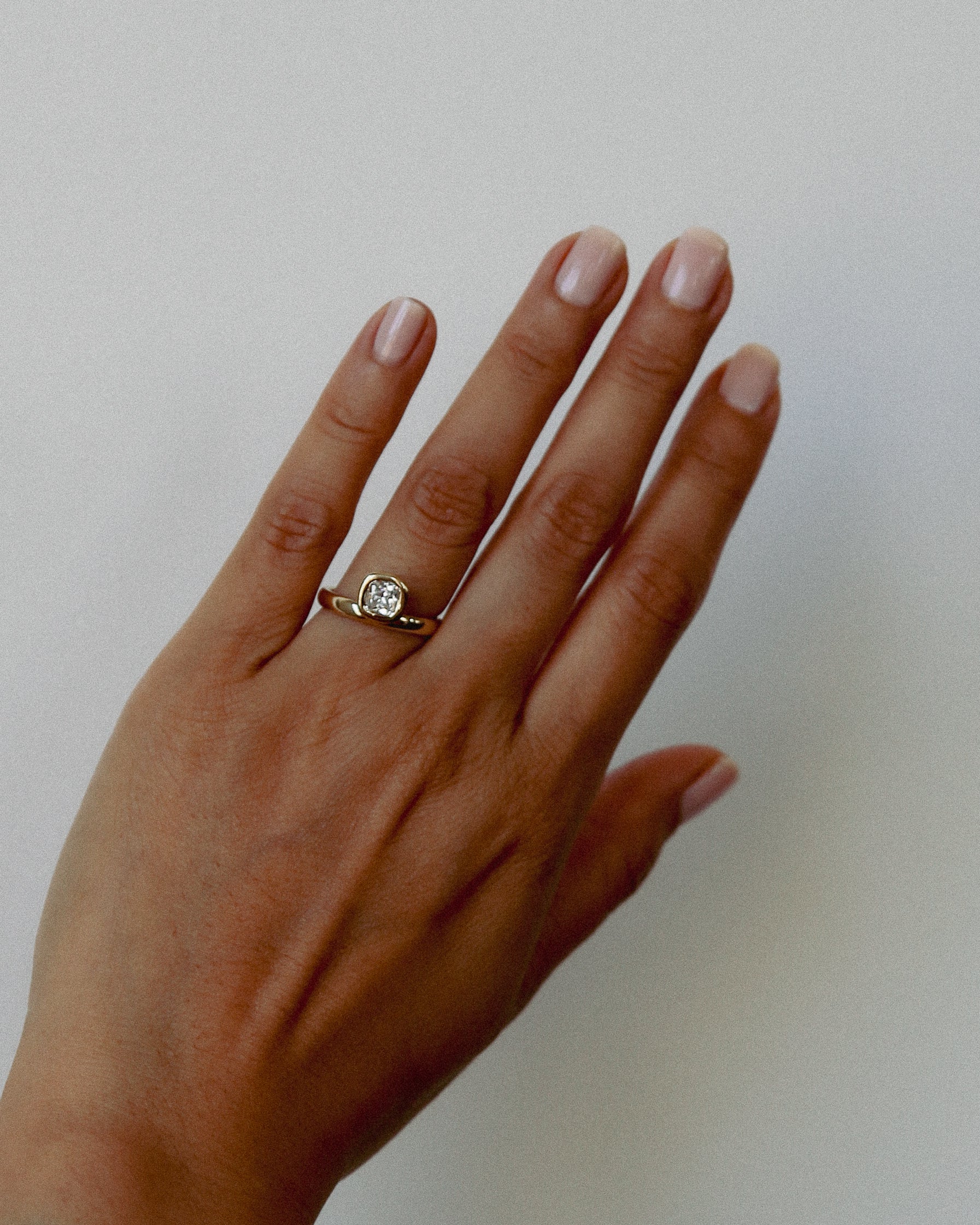 Hand wearing a ring with a diamond on a plain background