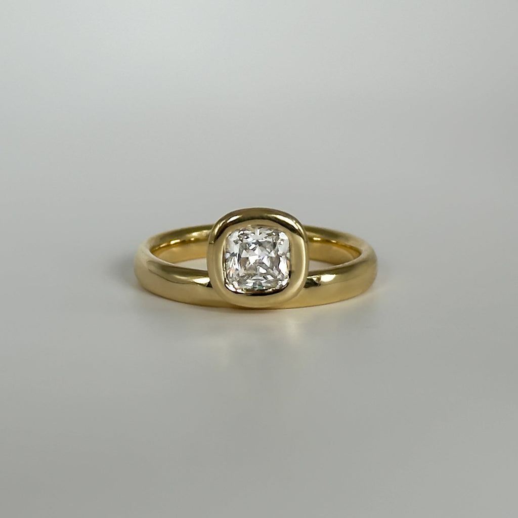 Gold ring with a cushion cut diamond on a light gray background
