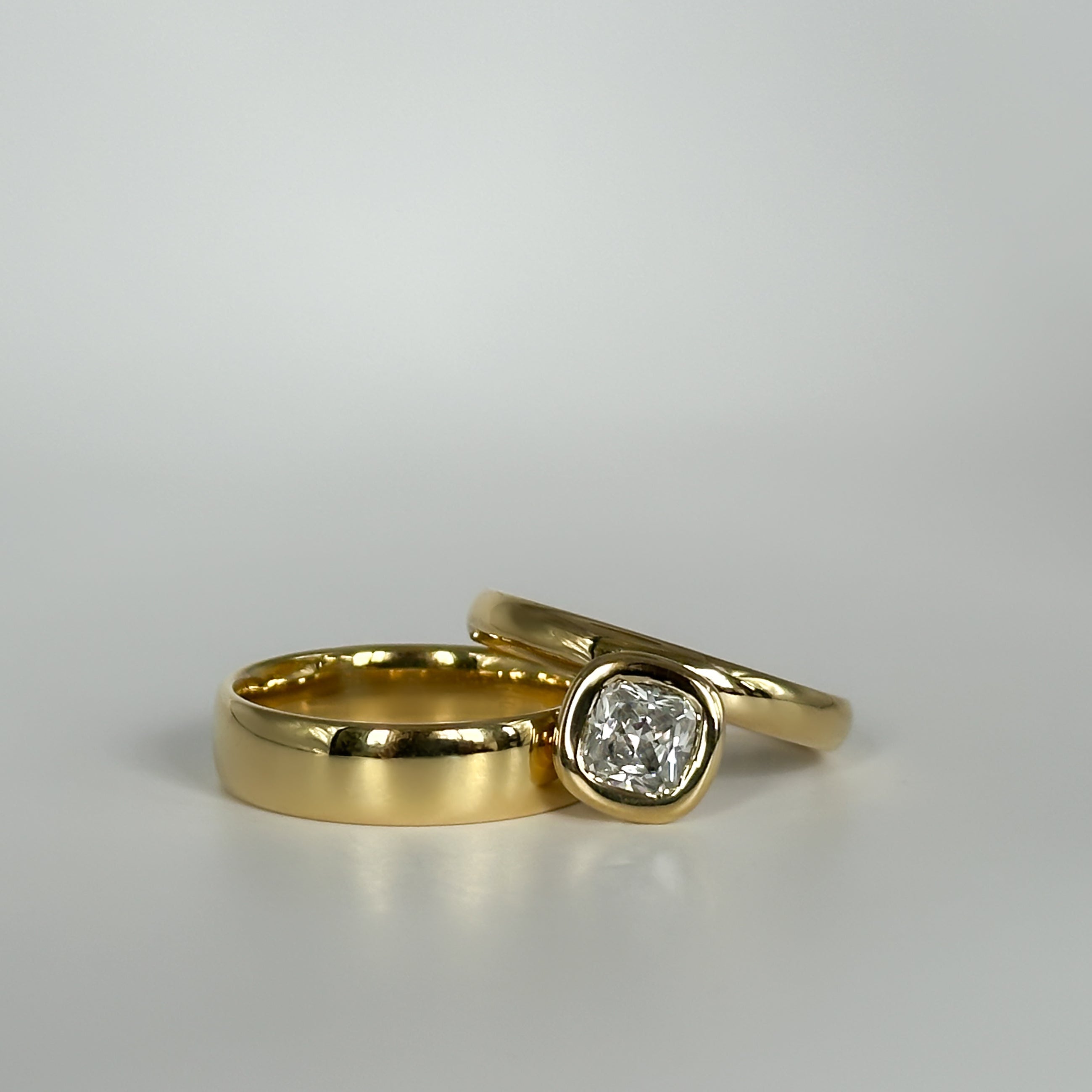 Two gold rings with one featuring a diamond on a light gray background