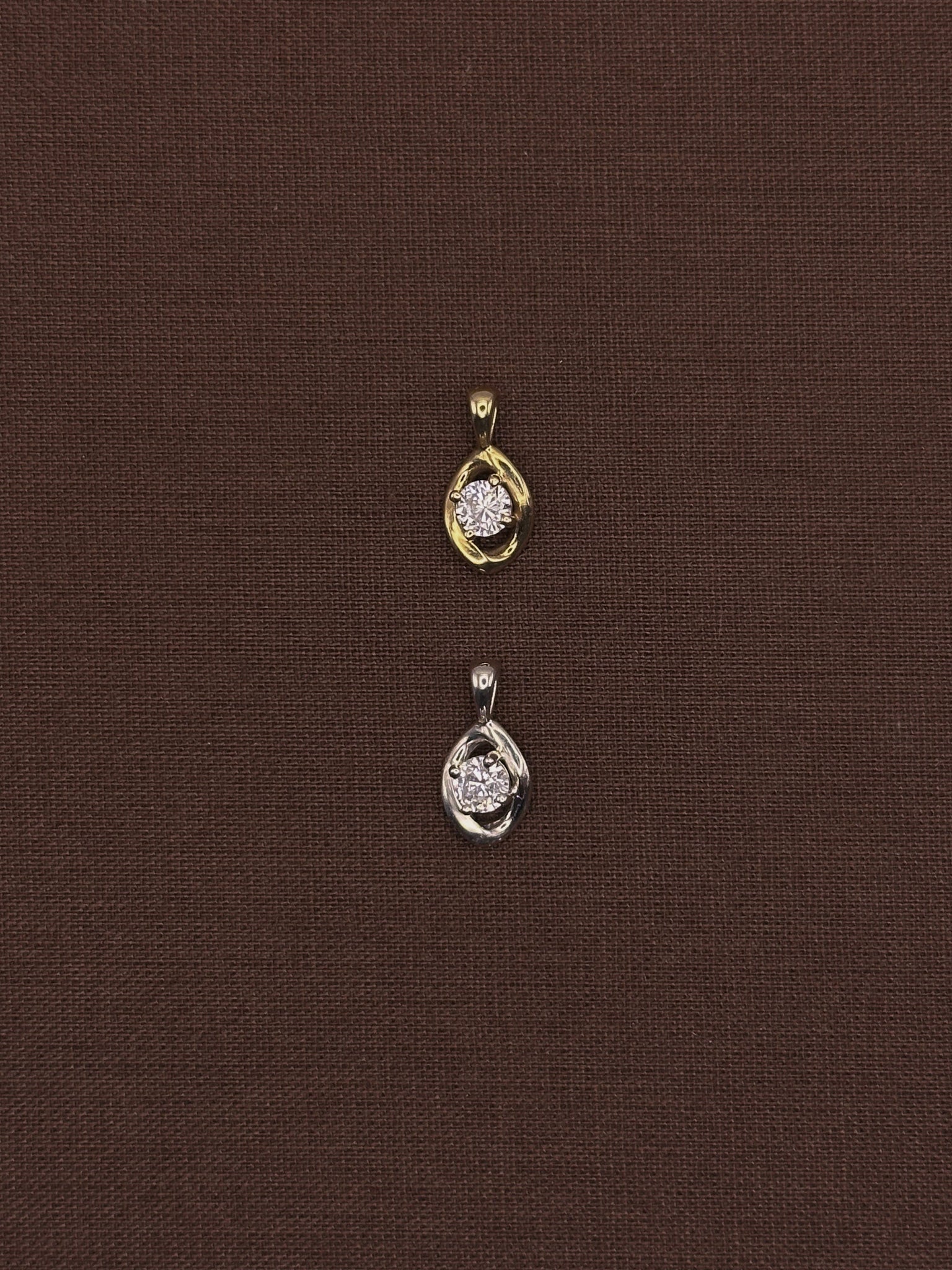 Two gold diamond pendants on a brown fabric background