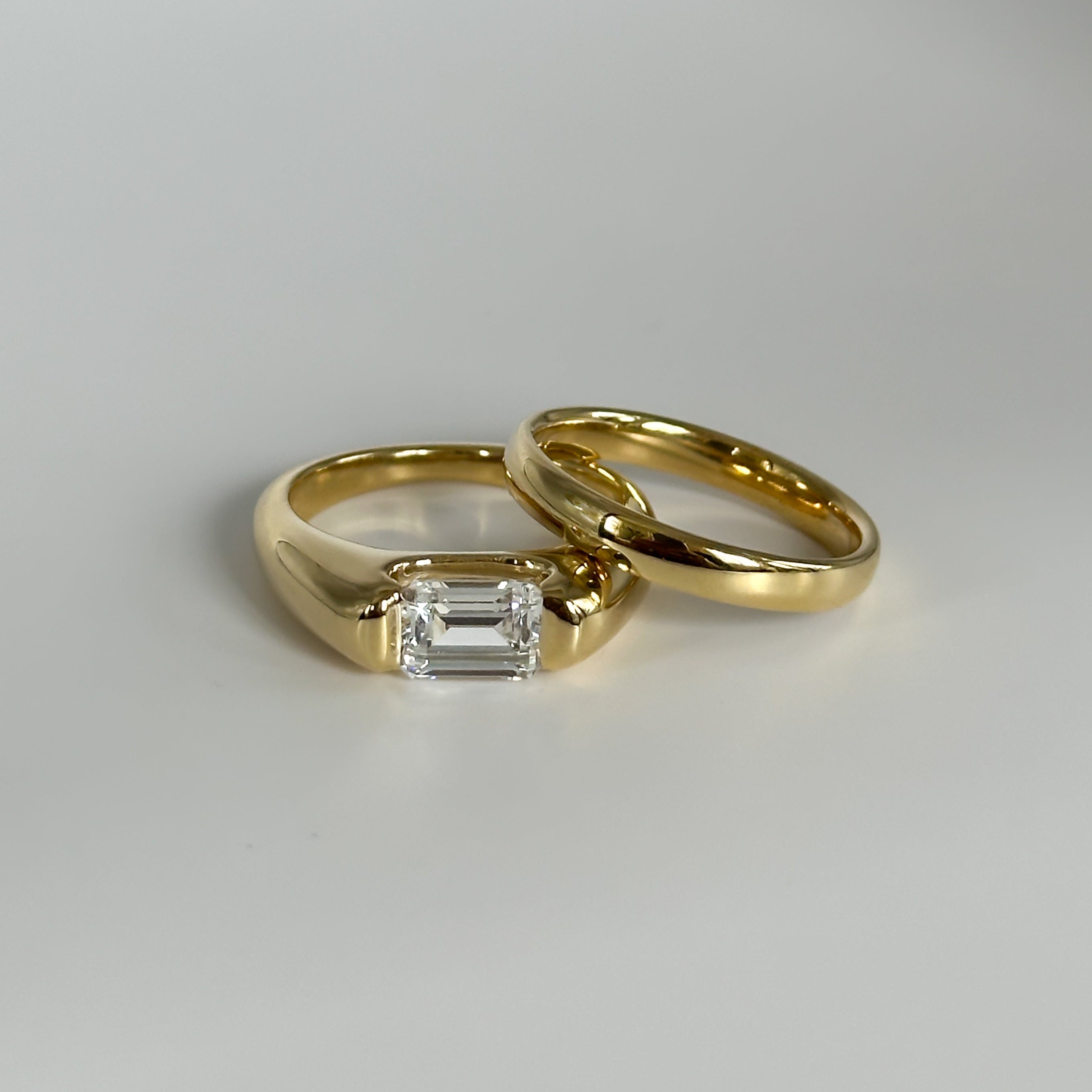 Two gold rings with a diamond on a light gray background