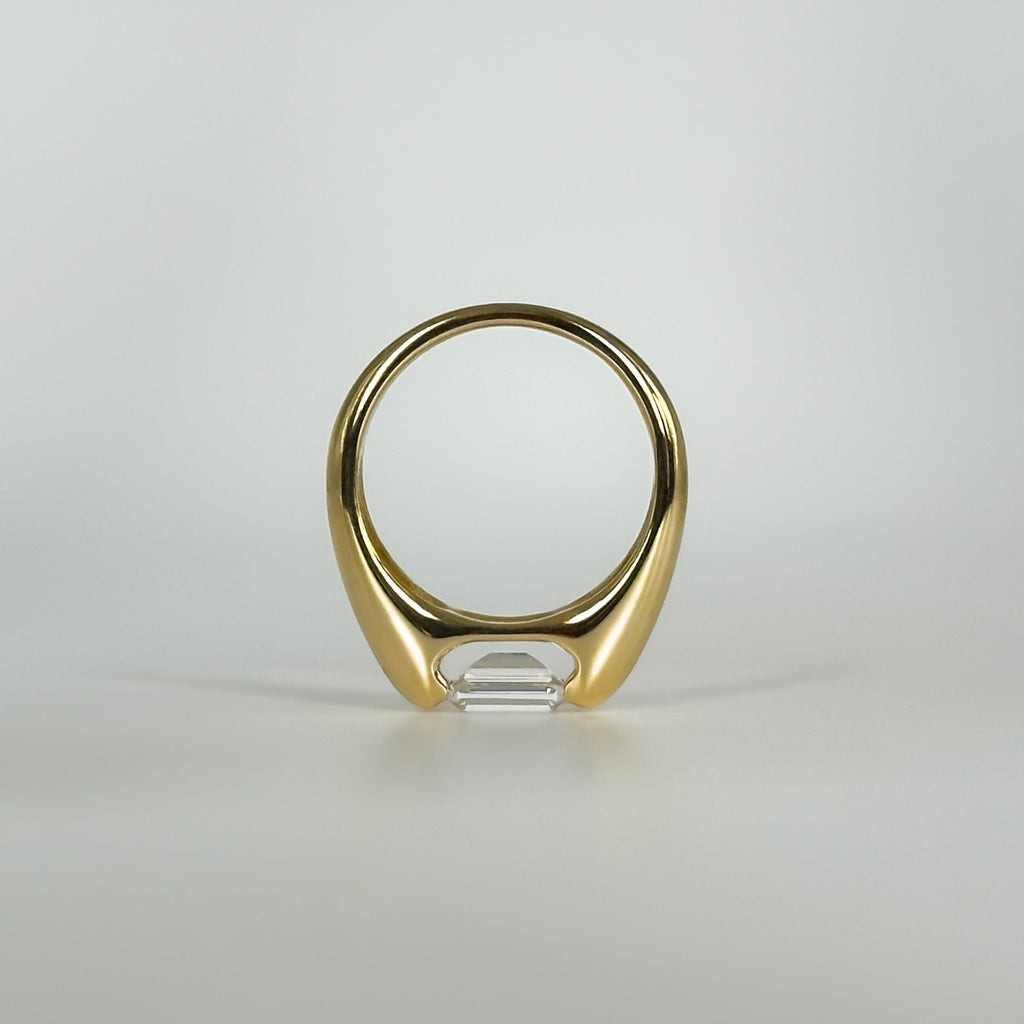 Gold ring with an emerald cut diamond on a light gray background