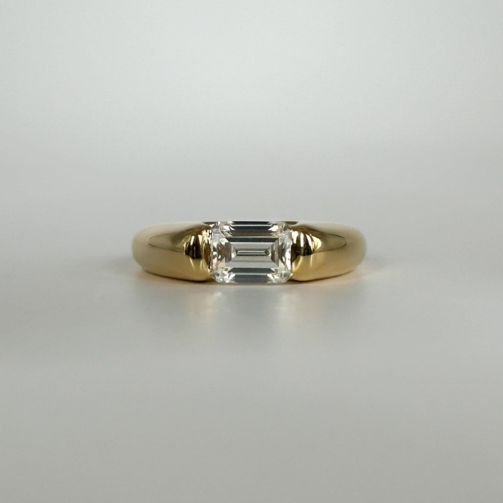 Gold ring with an emerald cut diamond on a light gray background