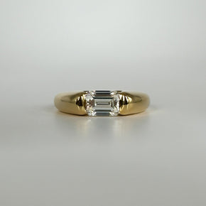 Gold ring with an emerald cut diamond on a light gray background