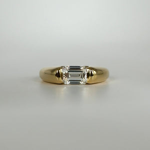 Gold ring with an emerald cut diamond on a light gray background