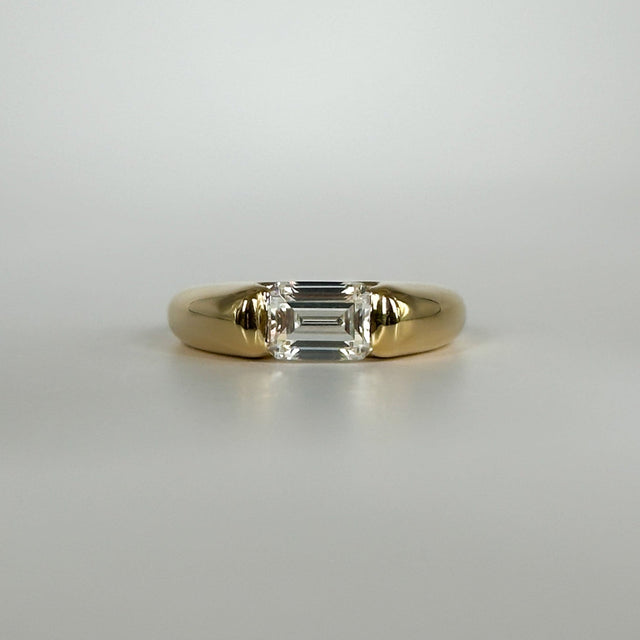 Gold ring with an emerald cut diamond on a light gray background