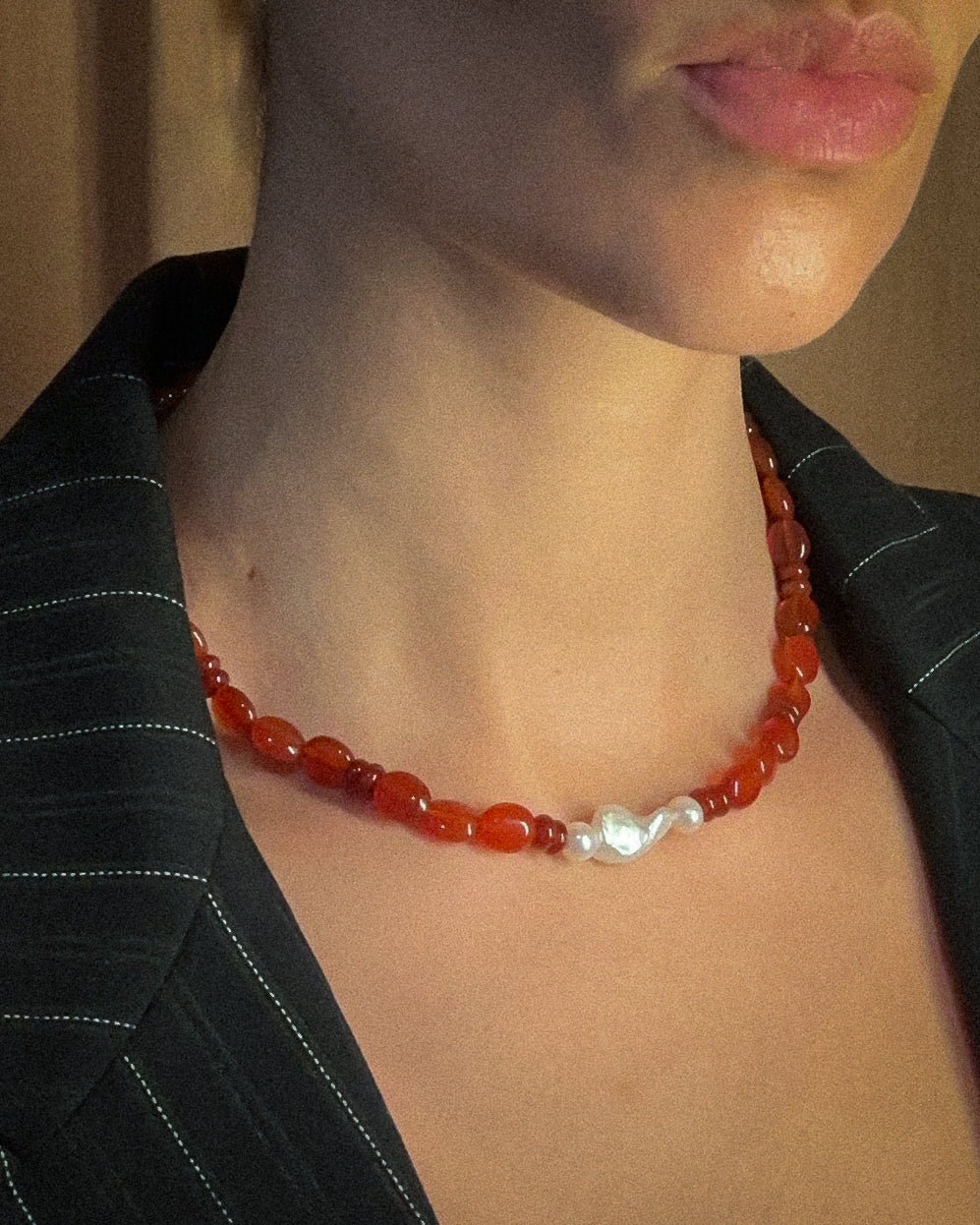 Person wearing a red beaded necklace with three white pearl accents.