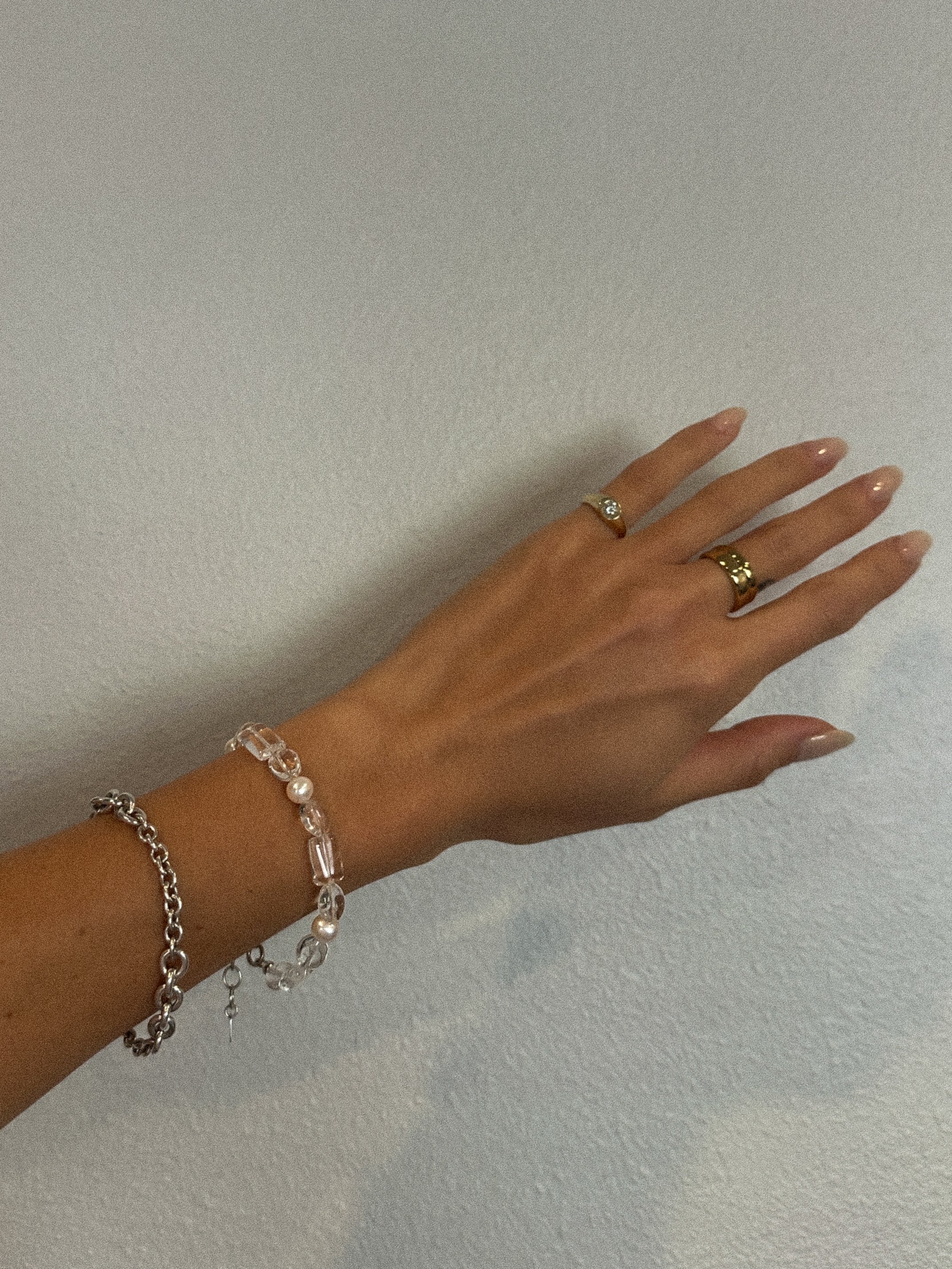 Hand wearing a bracelet and two rings on a plain background