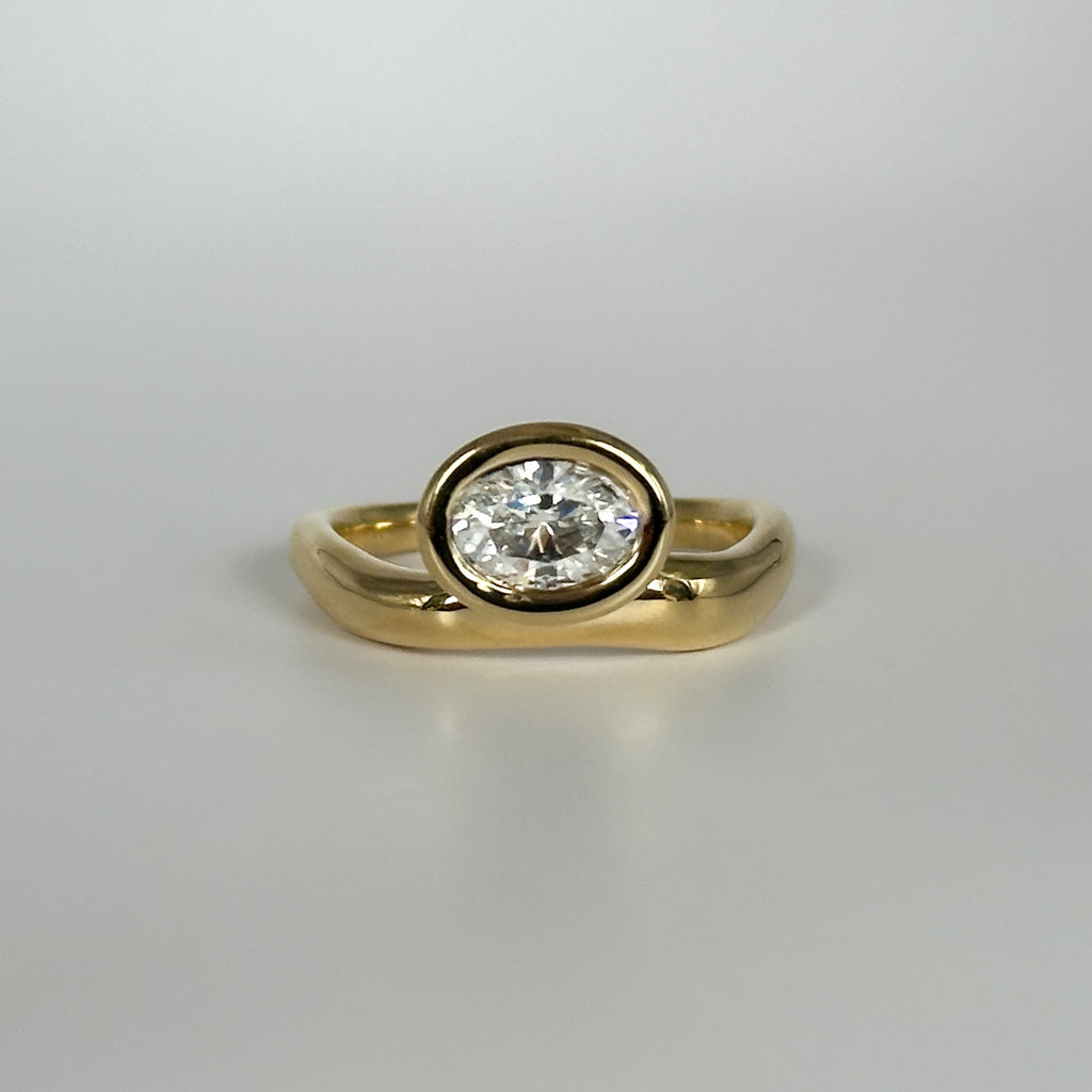 Gold ring with an oval-cut diamond on a light gray background