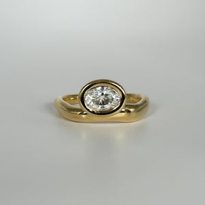 Gold ring with an oval-cut diamond on a light gray background