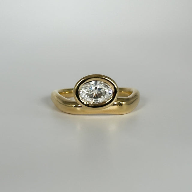 Gold ring with an oval-cut diamond on a light gray background