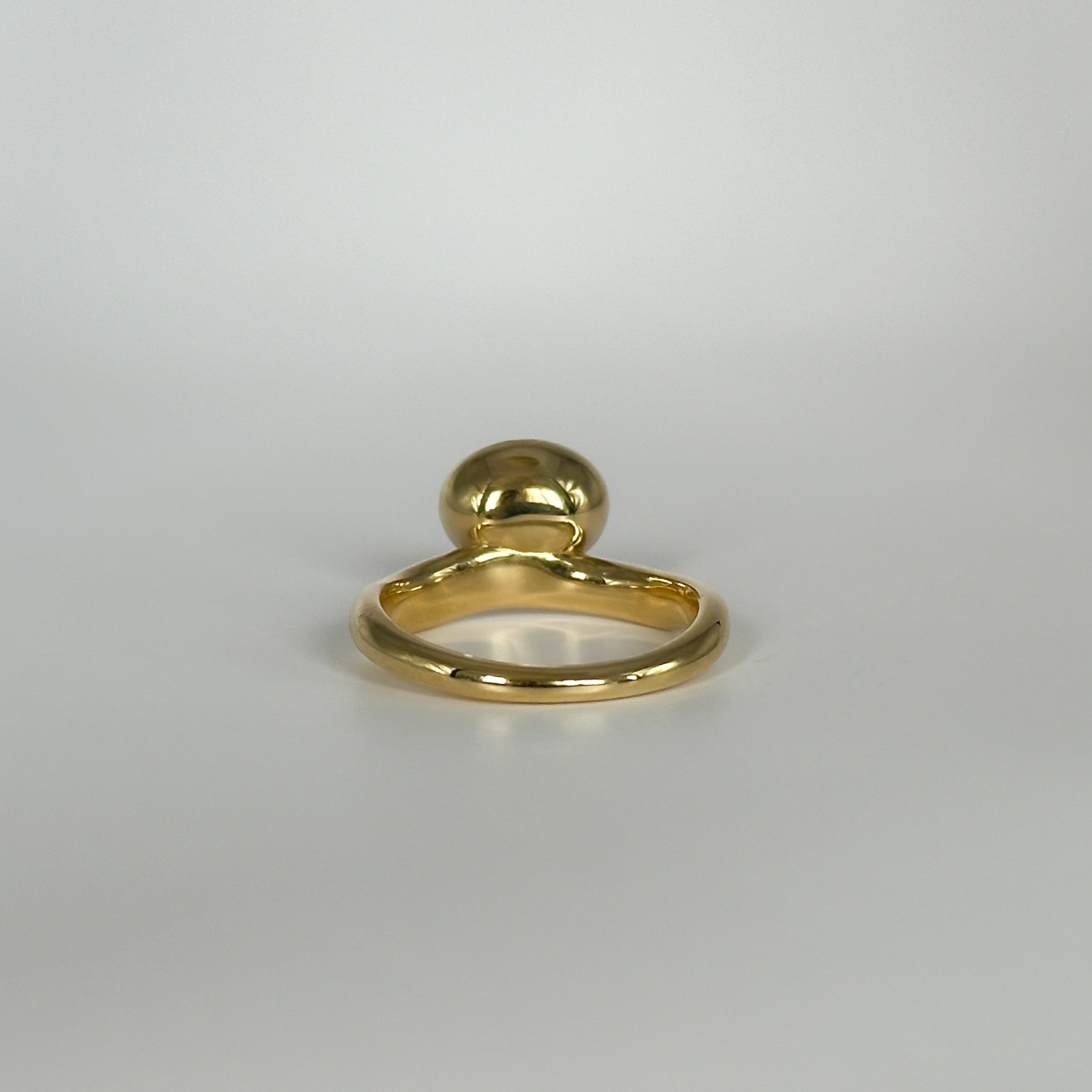 Gold ring with a spherical top on a light gray background