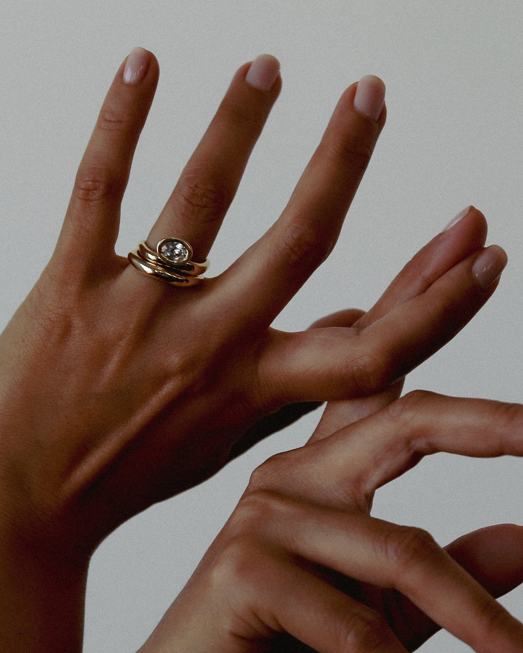 Close-up of a hand wearing a gold ring with a diamond on a neutral background