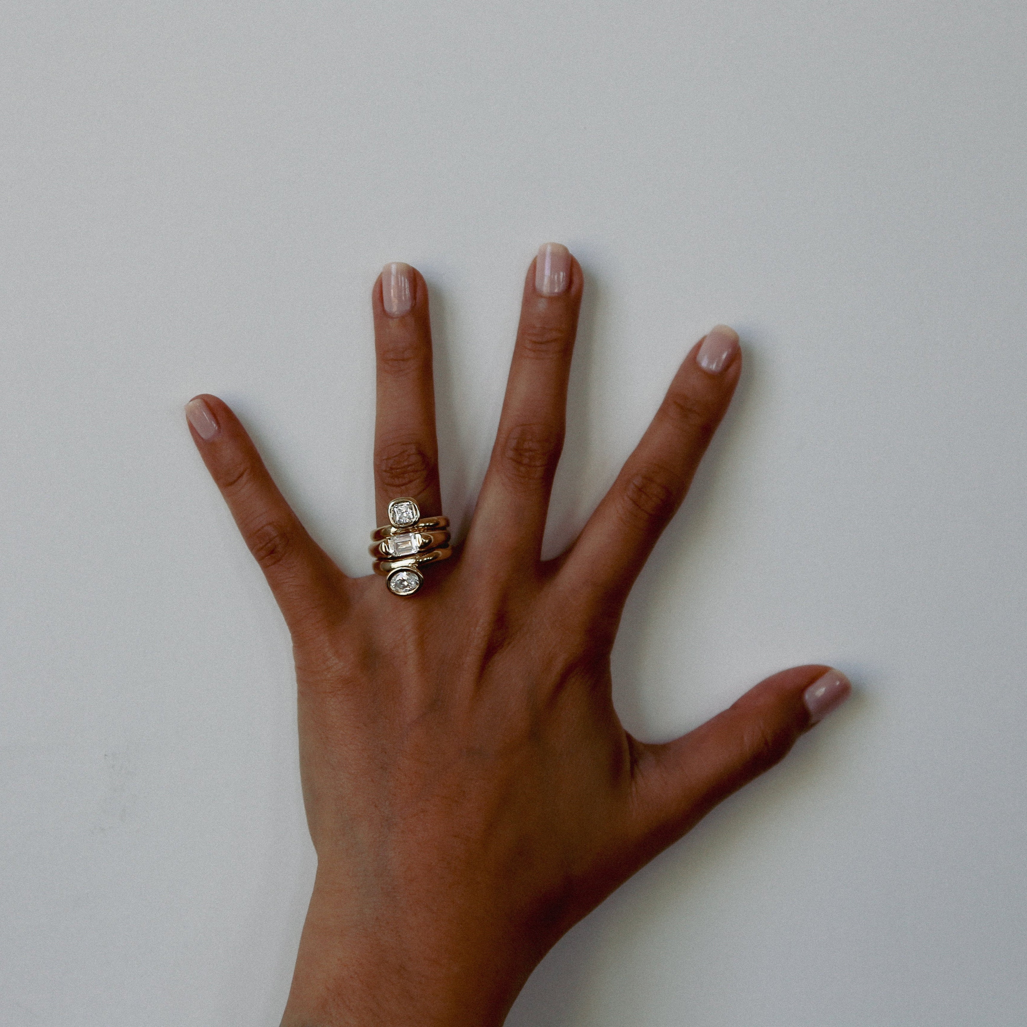 Hand with three stacked rings on a plain background
