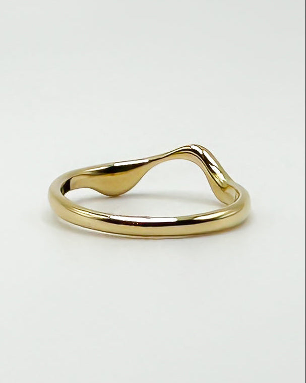 Backside of a polished gold ring with a wavy, organic ring on the upper band, photographed on a clean white background.