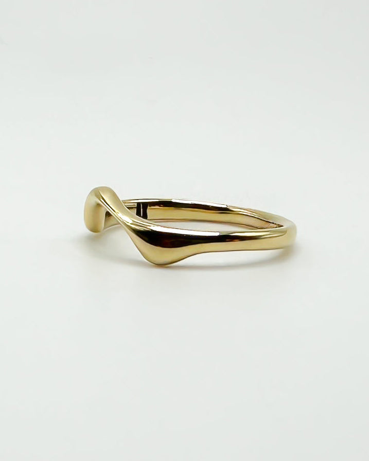 A polished gold ring with a unique, fluid wavy design, photographed on a clean white background.