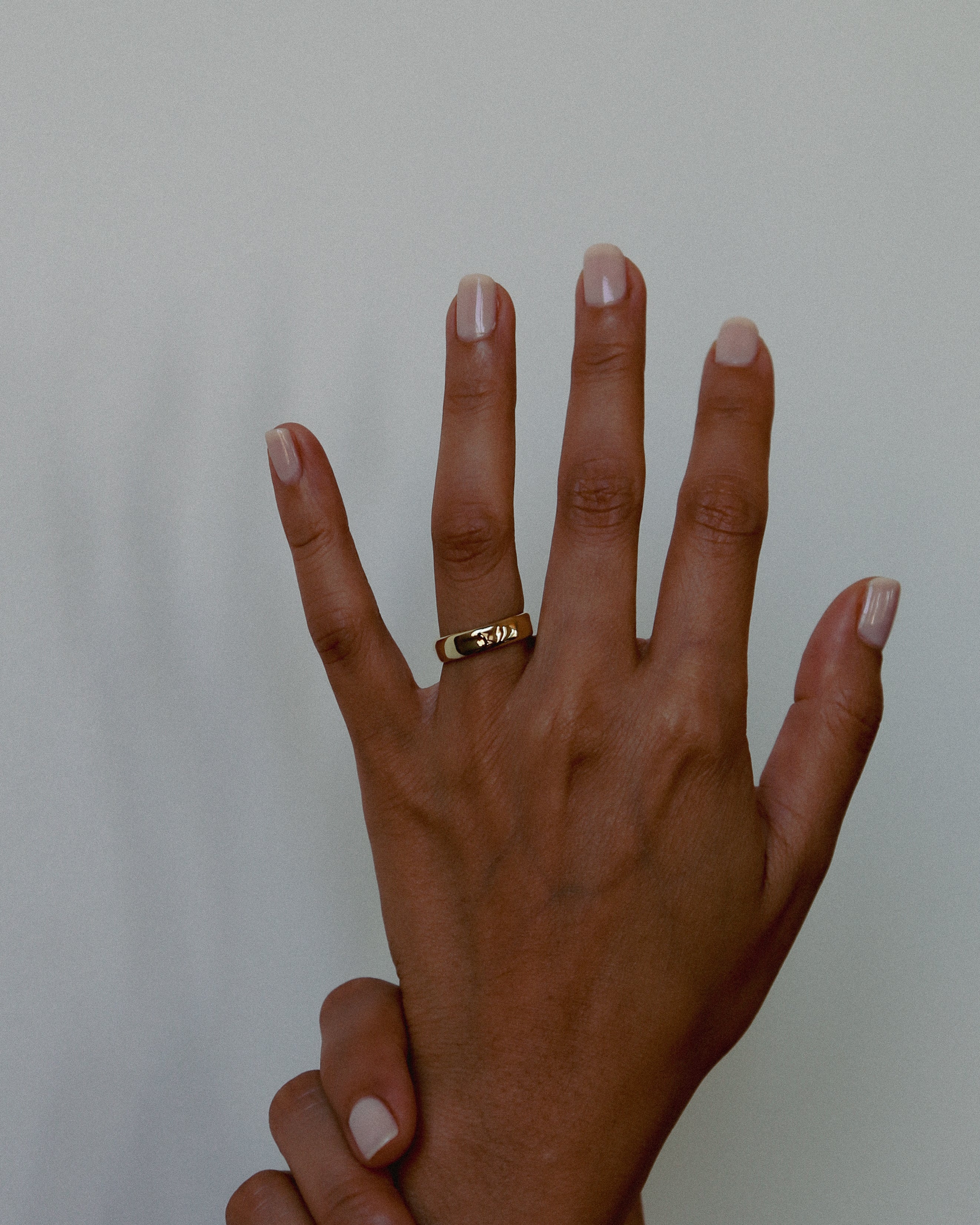 Hand wearing a gold ring on a plain background