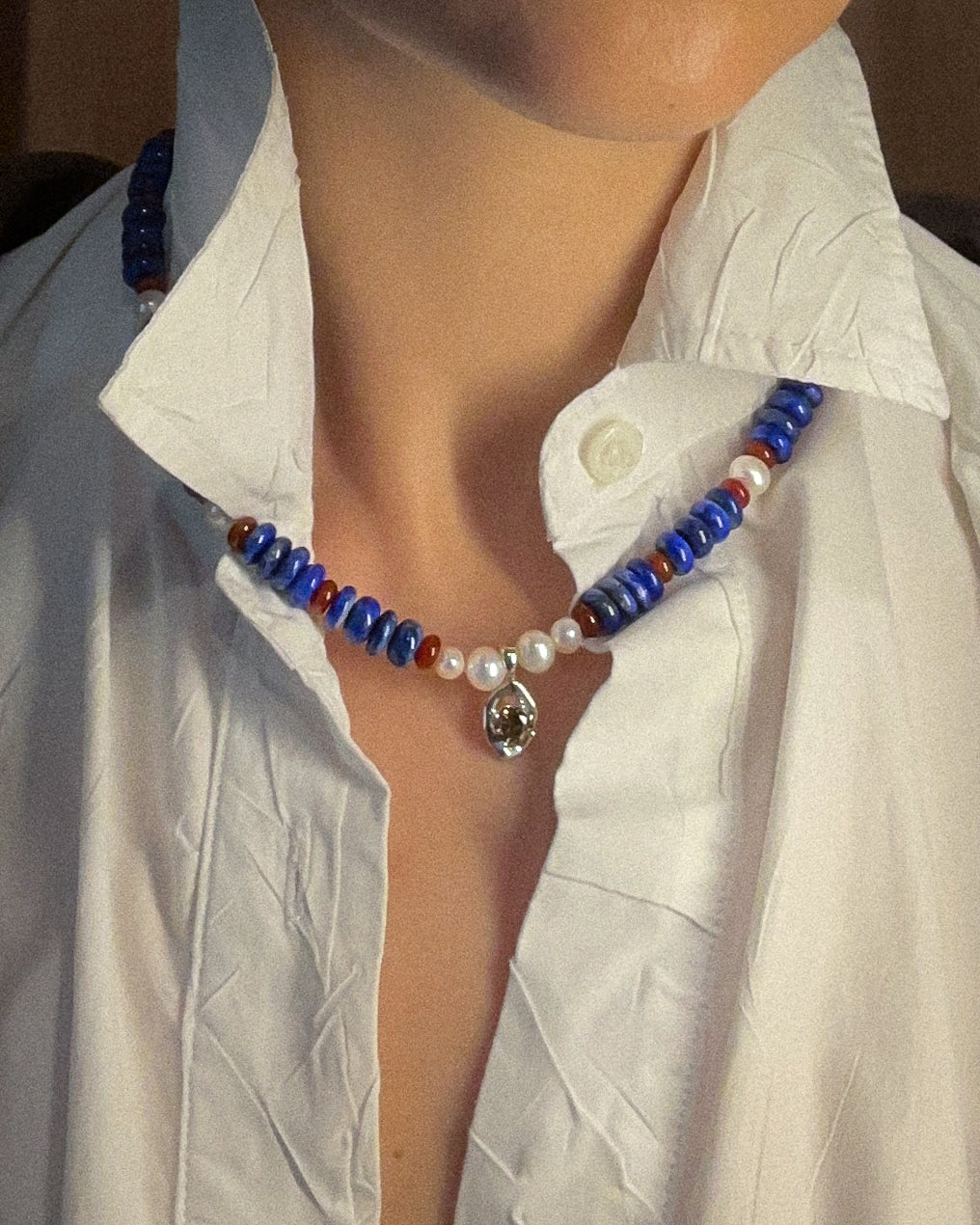 Necklace with blue and red beads and white pearls worn by a person in a white shirt.