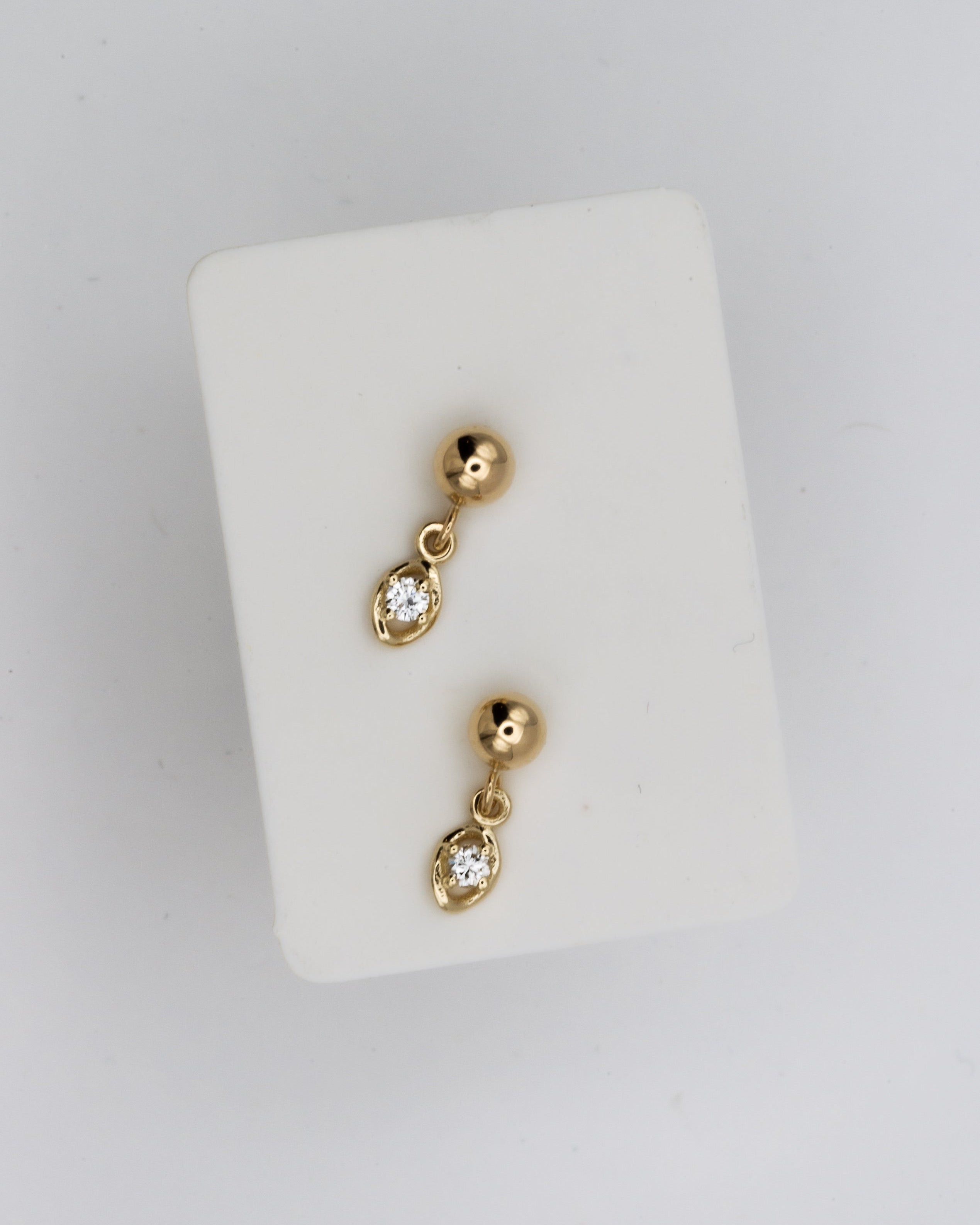 Gold earrings with small stones on a white stand against a light gray background
