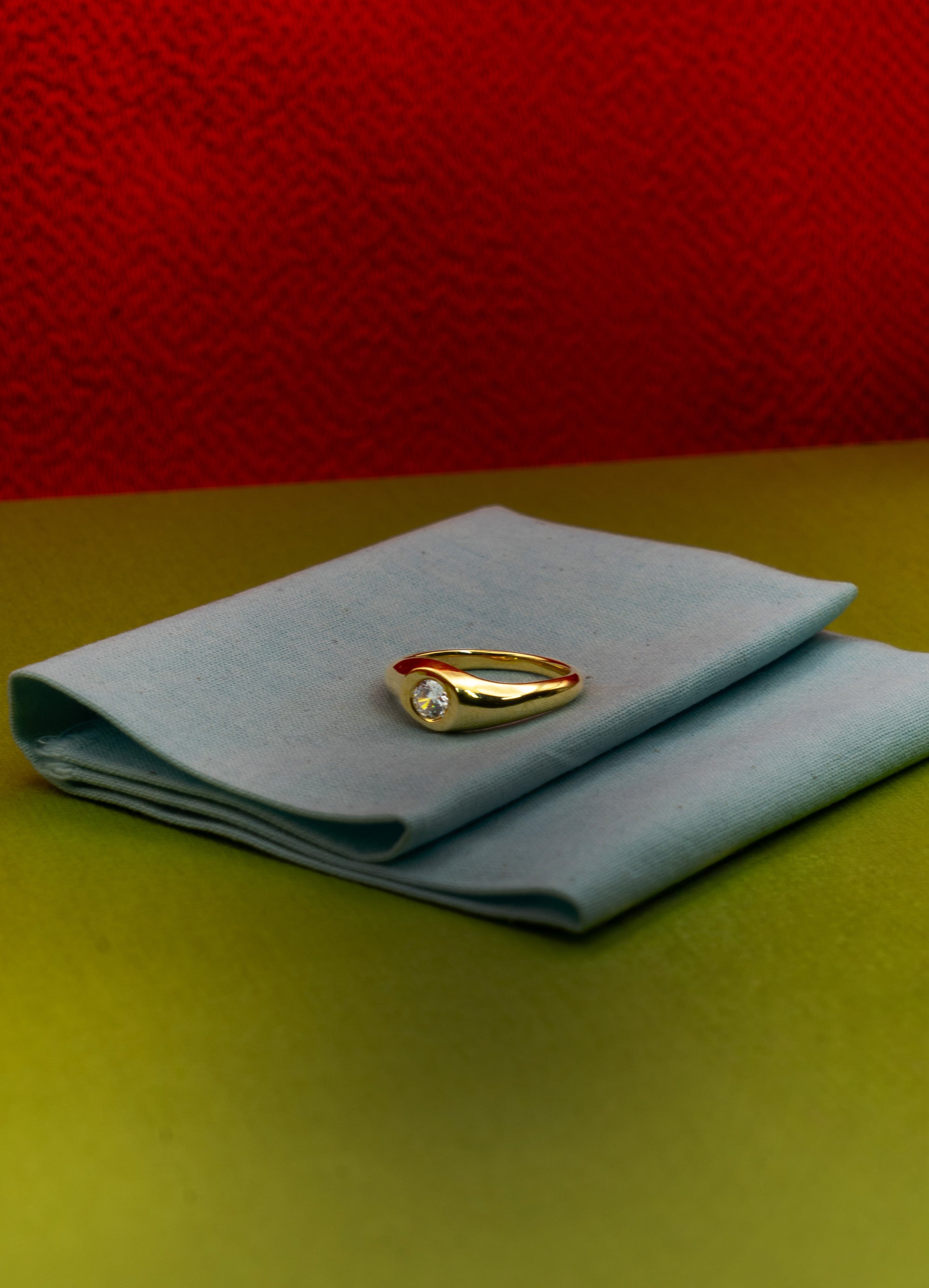 Gold ring on a light blue cloth against a red background